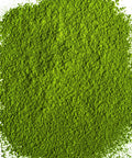 A mound of bright green matcha powder scattered on a plain white background.