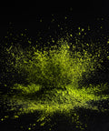 A dramatic burst of bright neon yellow-green powder or pigment splashing and settling against a solid black background.